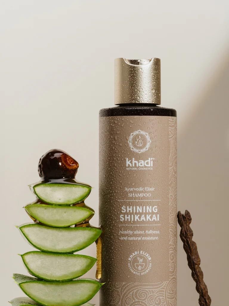 Khadi Shining Shikakai Shampoo-Flasche mit Deckel. Neben Aloe Vera und einem Holzstück. Text: Ayurvedisches Elixier, natürliche Feuchtigkeit.