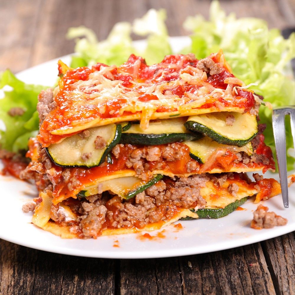 Lasagne auf Teller. Schichten aus Nudeln, Hackfleisch, Zucchini und Käse. Salatbeilage.