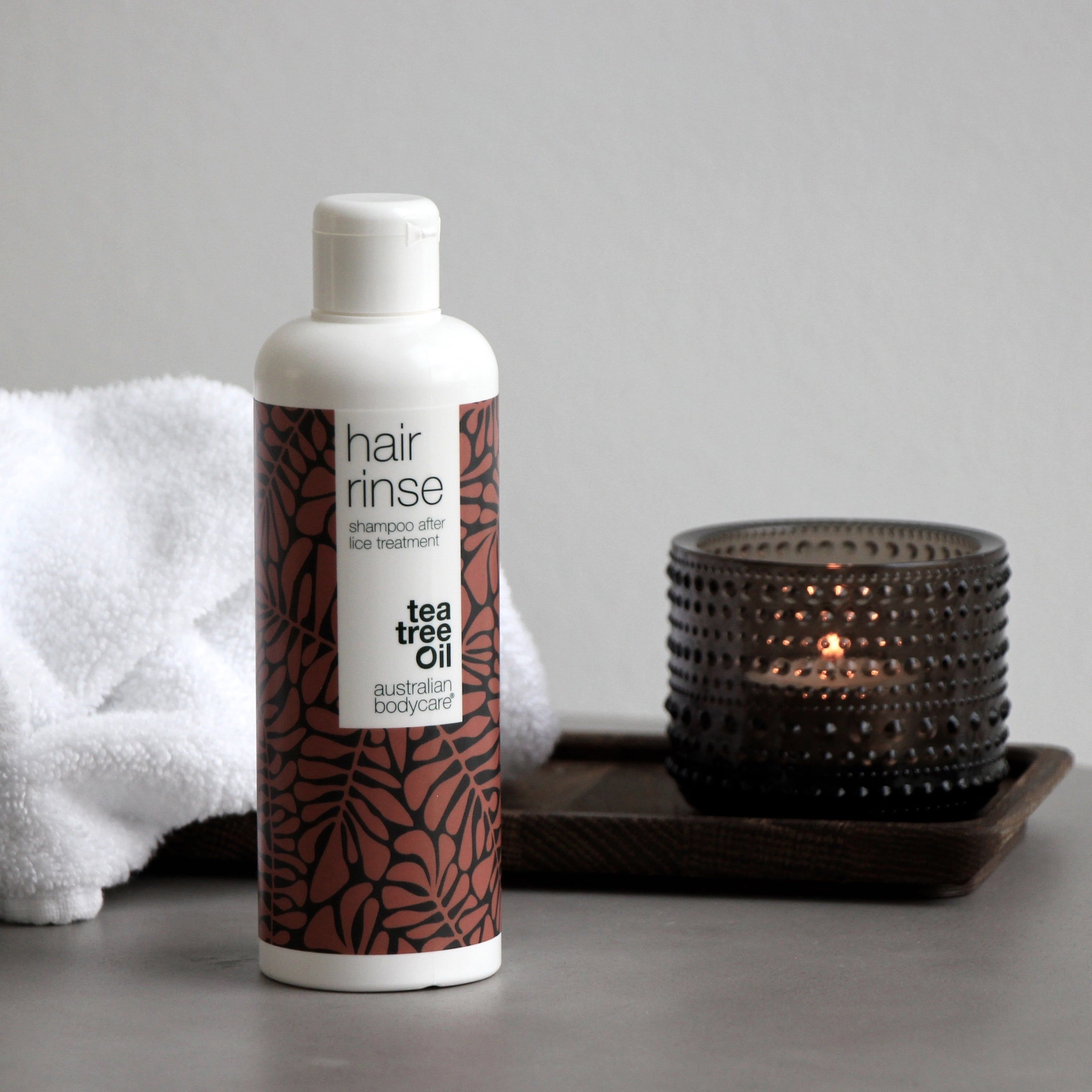 Flasche mit braunem Blattmuster, Handtuch und Kerze. Aufschrift: hair rinse, Tea Tree Oil, australian bodycare.