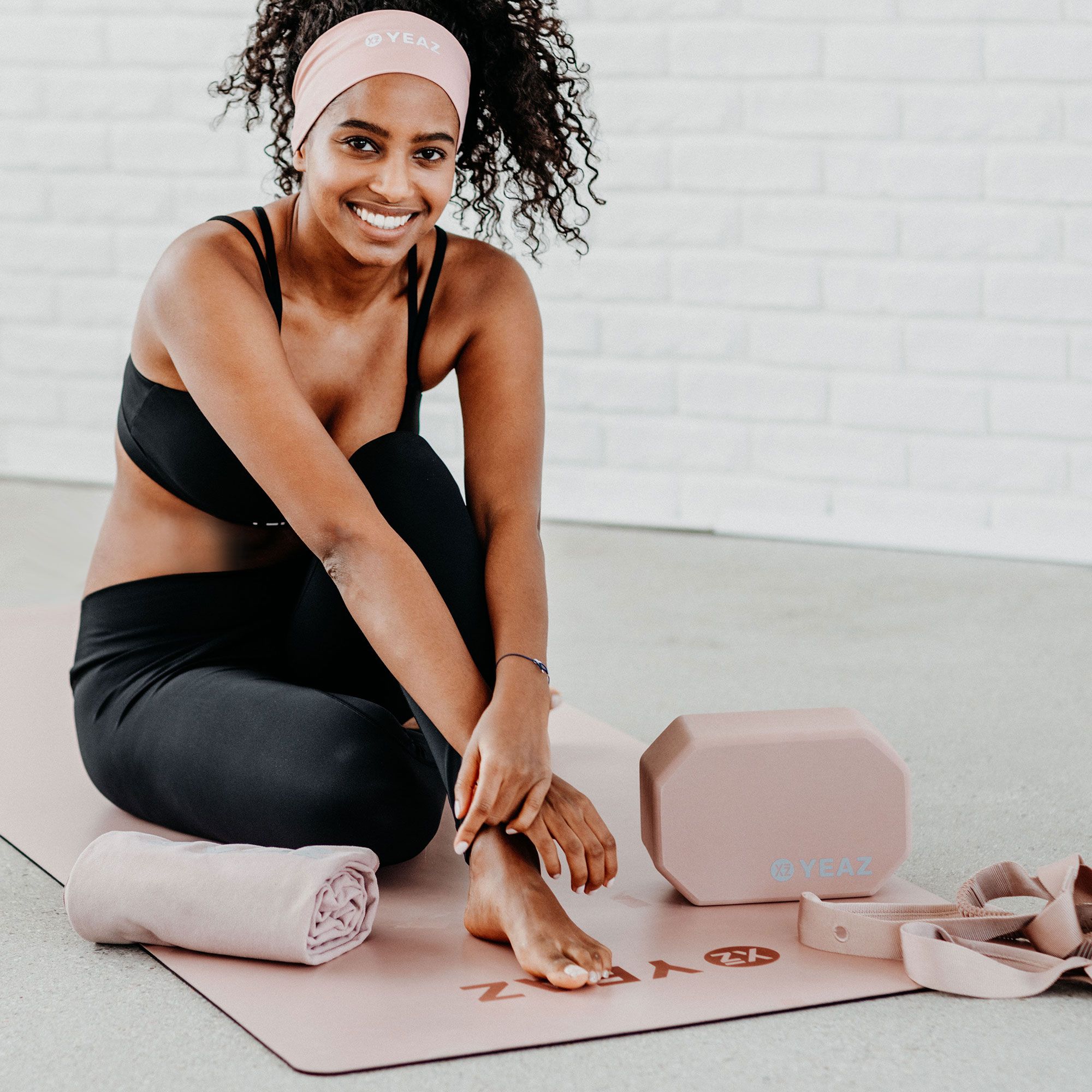Frau auf Yogamatte mit YEAZ-Produkten: Block, Band und Handtuch.