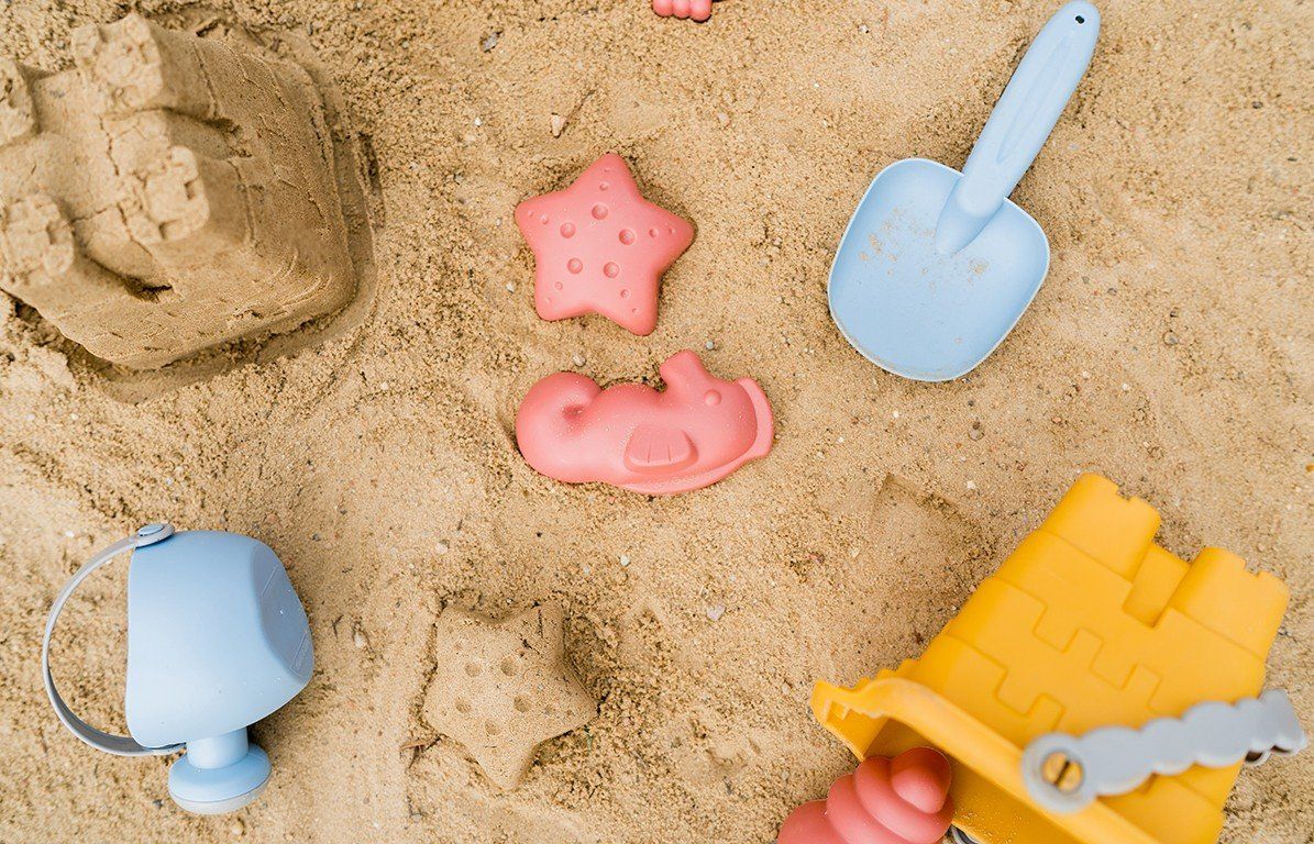 Sandspielzeug mit gelbem Eimer, blauer Gießkanne, Schaufel und rosa Formen. Sandspielzeug auf Sand.