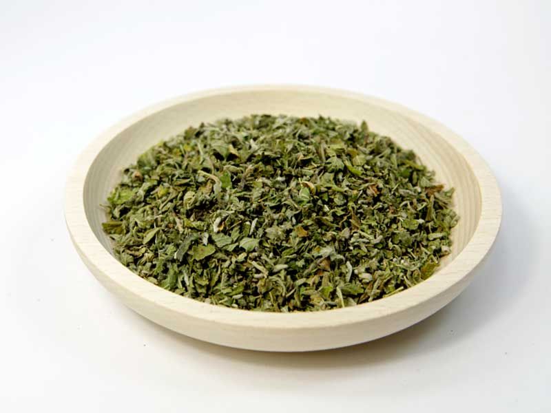 Getrocknete, zerkleinerte Kräuter in einer runden Holzschale. Helle Holzfarbe, Kräuter grün.