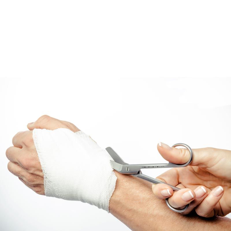 Chirurgische Schere schneidet Verbandsmaterial an einem Arm.