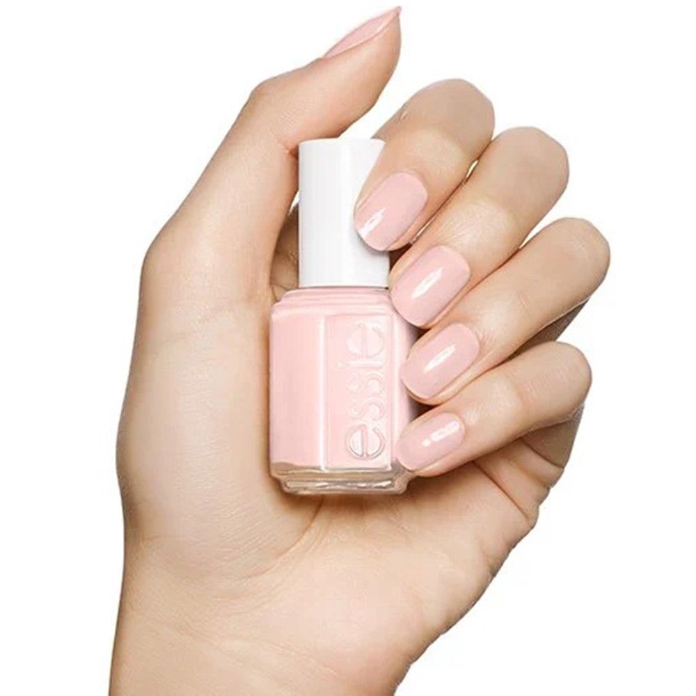 Eine Hand hält eine Flasche hellrosa Nagellack mit weißem Deckel. Die Nägel sind ebenfalls hellrosa lackiert.