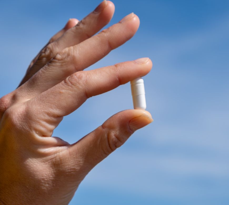 Hand hält eine einzelne Magnesiumcitrat Kapsel vor blauem Himmel.