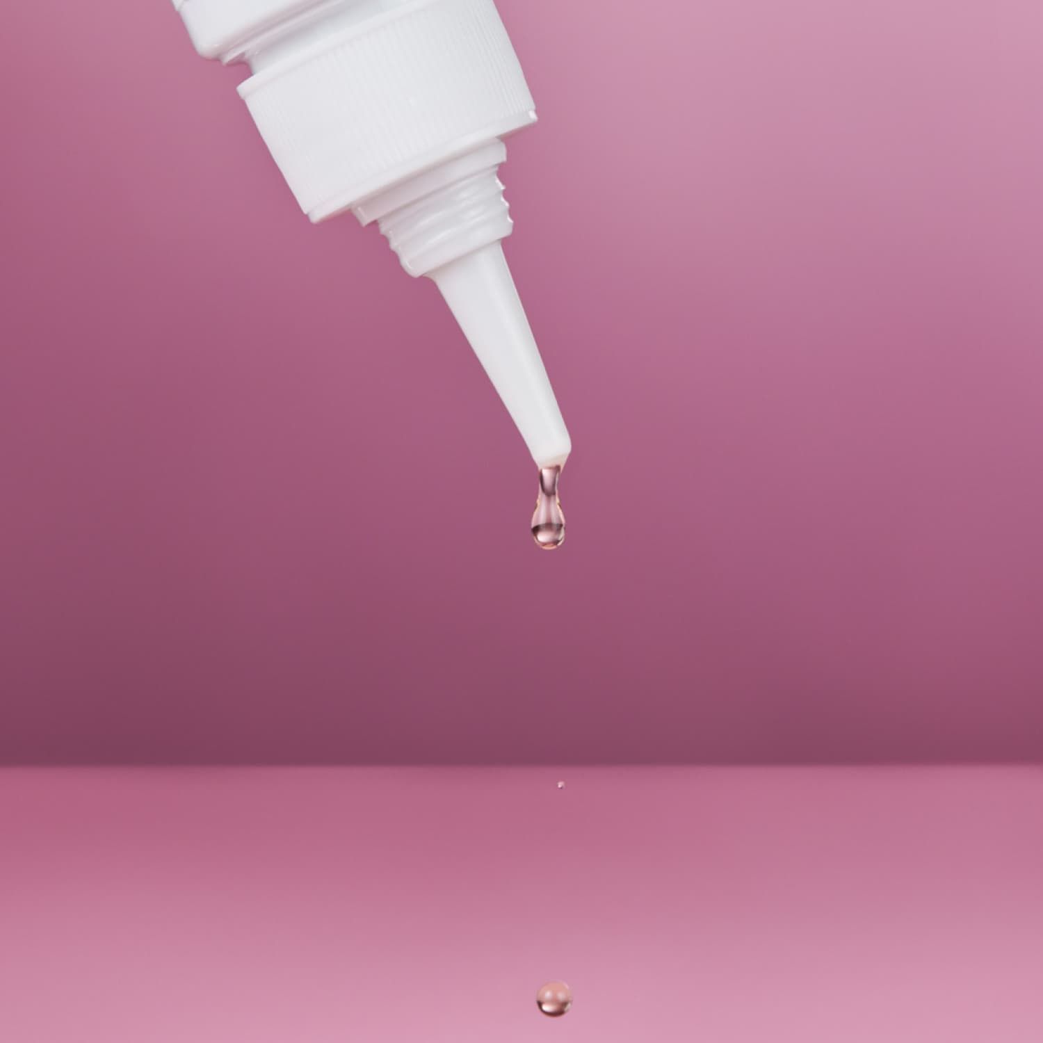 Weiße Flasche mit Tropfspitze. Ein Tropfen Flüssigkeit fällt herab.