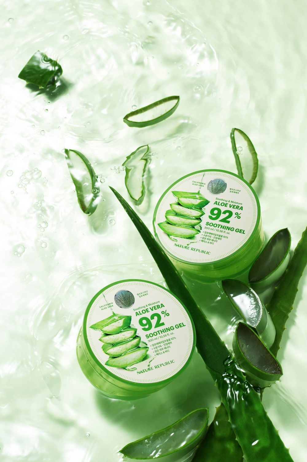 Zwei grüne Tiegel im Wasser, umgeben von Aloe Vera-Blättern. Aufkleber mit Text: "Soothing & Moisture Aloe Vera 92% Soothing Gel".