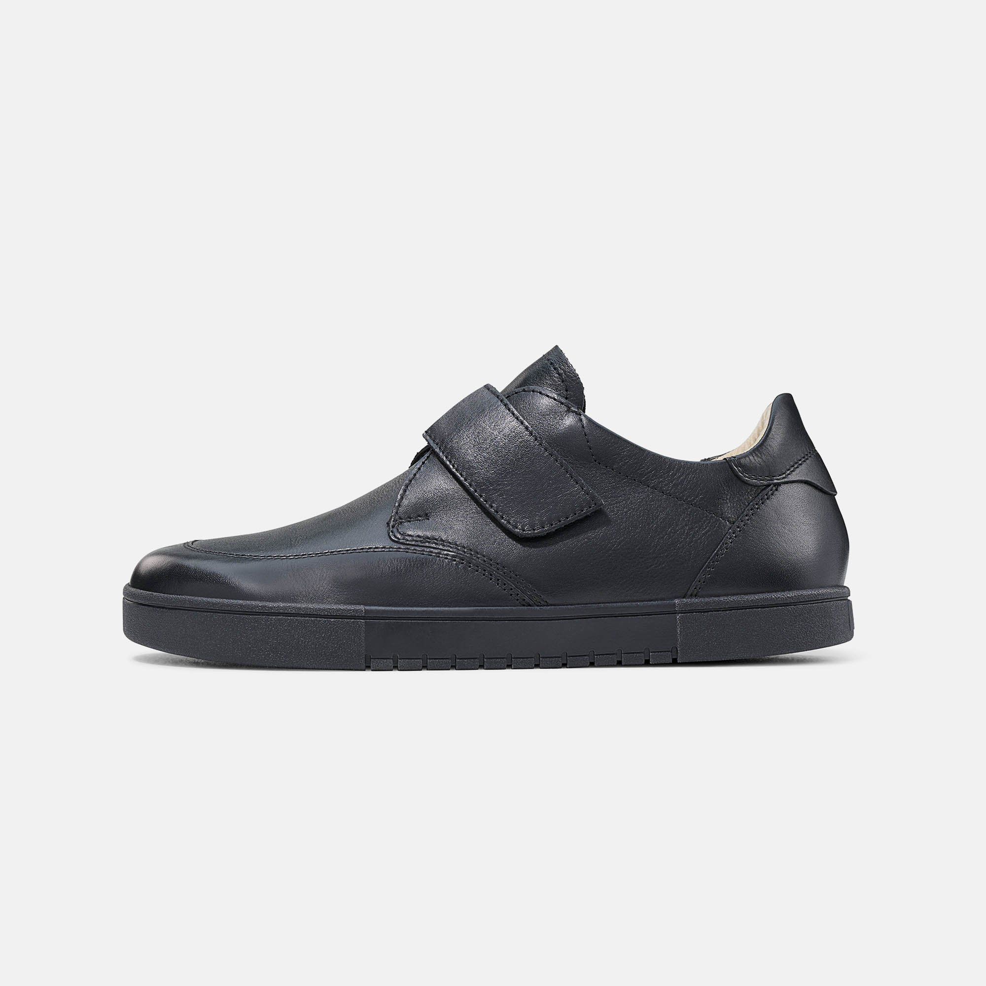 Schwarzer Herren-Slipper mit Klettverschluss. Glattes Leder. Gummisohle. Breite Passform. Seitenansicht.