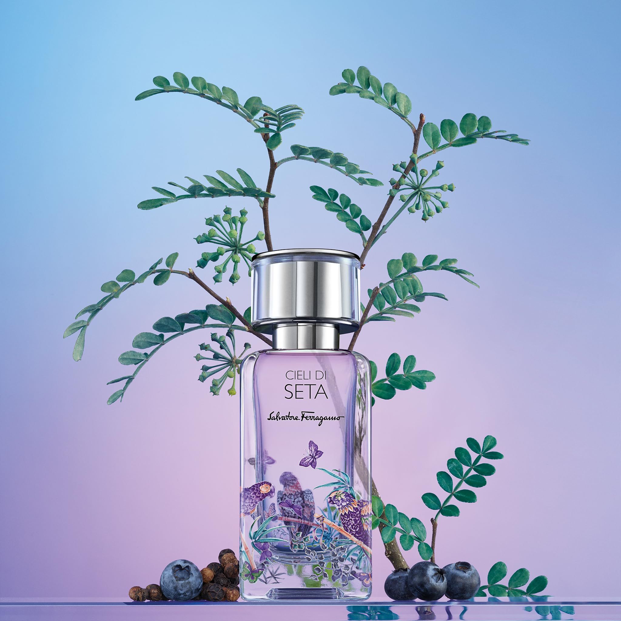 Salvatore Ferragamo Cieli di Seta EdP Nat. Spray. Flakon vor floralem Hintergrund mit Blättern, Beeren und Schmetterlingen.