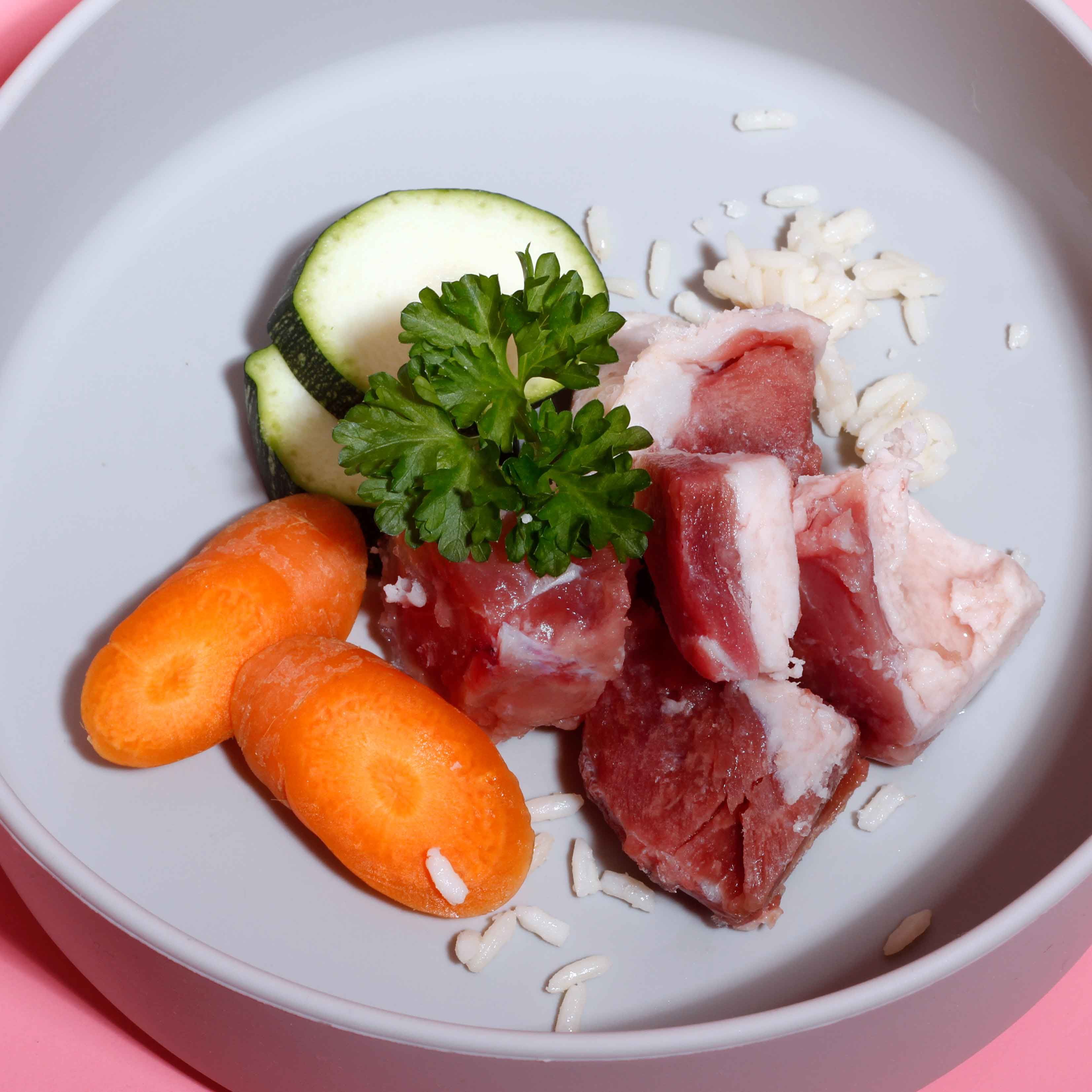 Graue Schale mit Gemüse, Fleisch und Reis. Karotten, Zucchini, Fleischstücke und Reis. Draufsicht.