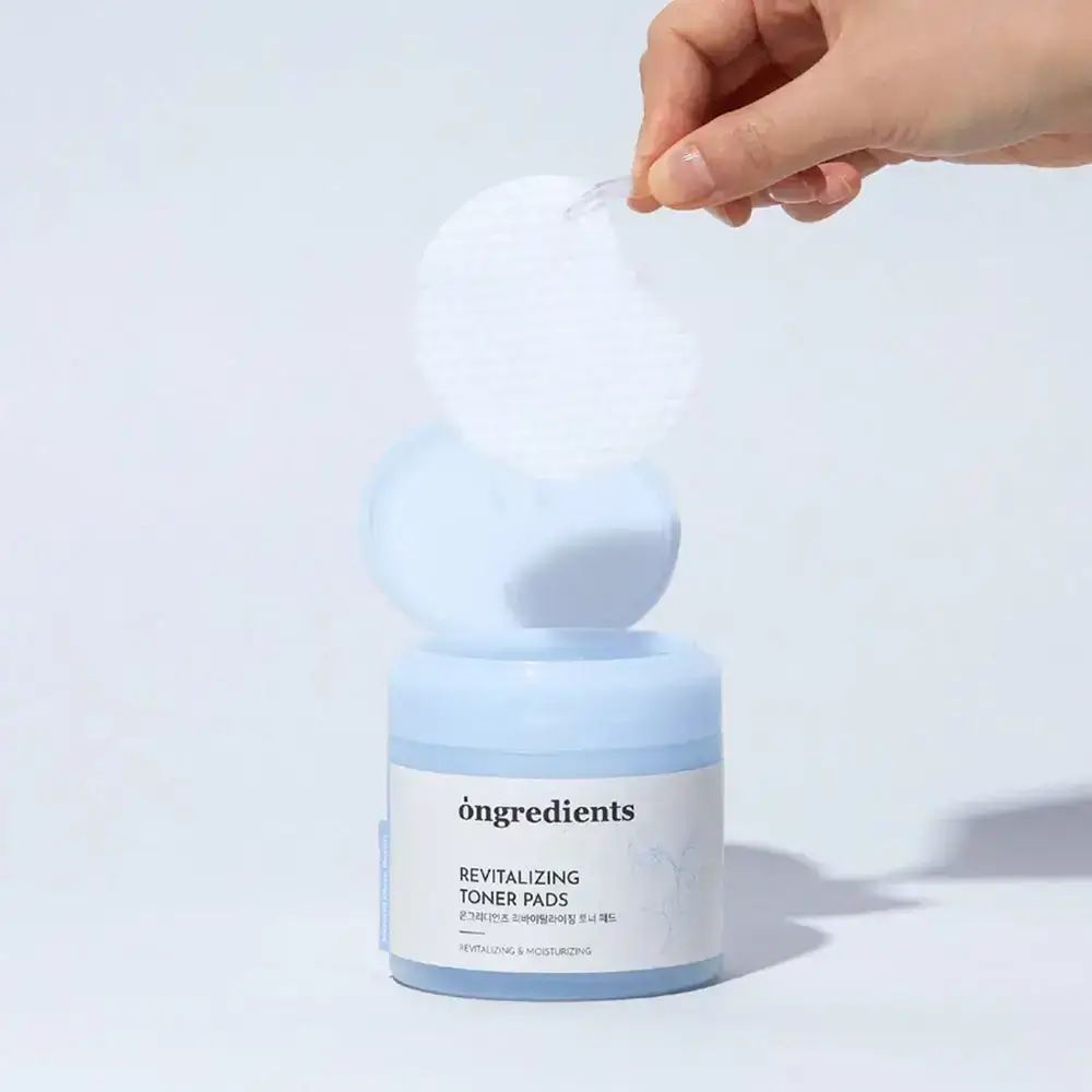 Geöffnete Dose mit Pads, Hand entnimmt Pad. Aufschrift: "ongredients Revitalizing Toner Pads".