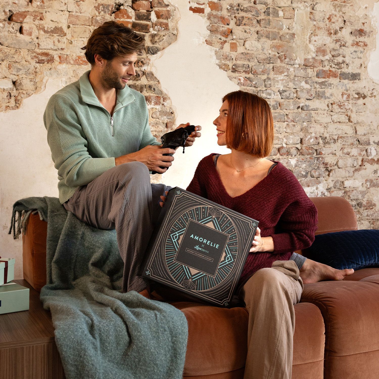 Ein Mann und eine Frau sitzen zusammen. Die Frau hält eine Adventskalender-Box. AMORELIE-Logo sichtbar.