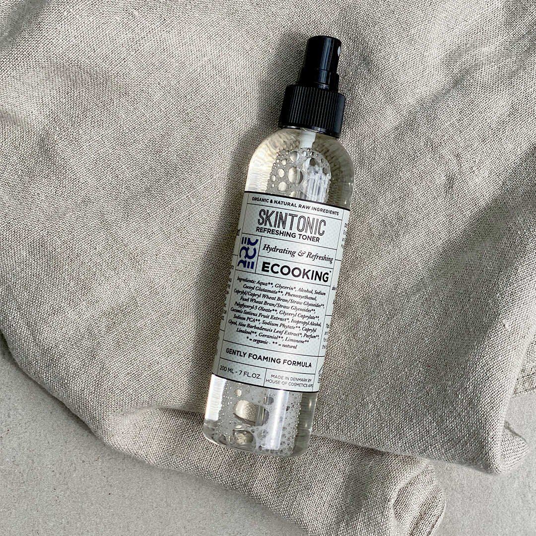 Eine Flasche Skin Tonic mit schwarzem Sprühkopf. Etikett mit Produktnamen und Marke Ecooking. Auf hellem Stoff.