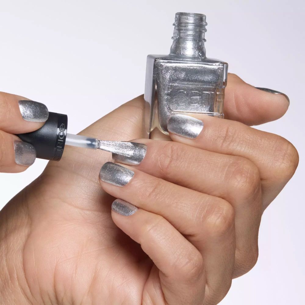 Hand mit silber lackierten Nägeln. Nagellack wird auf einen Nagel aufgetragen. Flasche sichtbar.