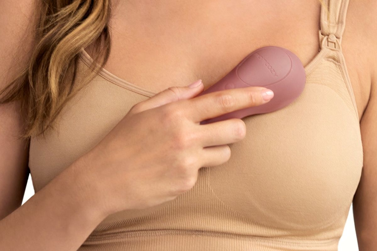 Person hält rosa Momcozy-Massagegerät an der Brust. Person trägt BH.