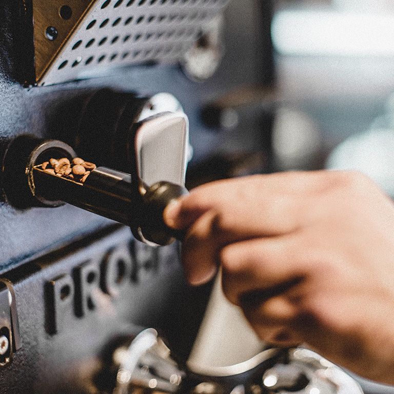Eine Hand entnimmt Kaffeebohnen aus einer Röstmaschine.