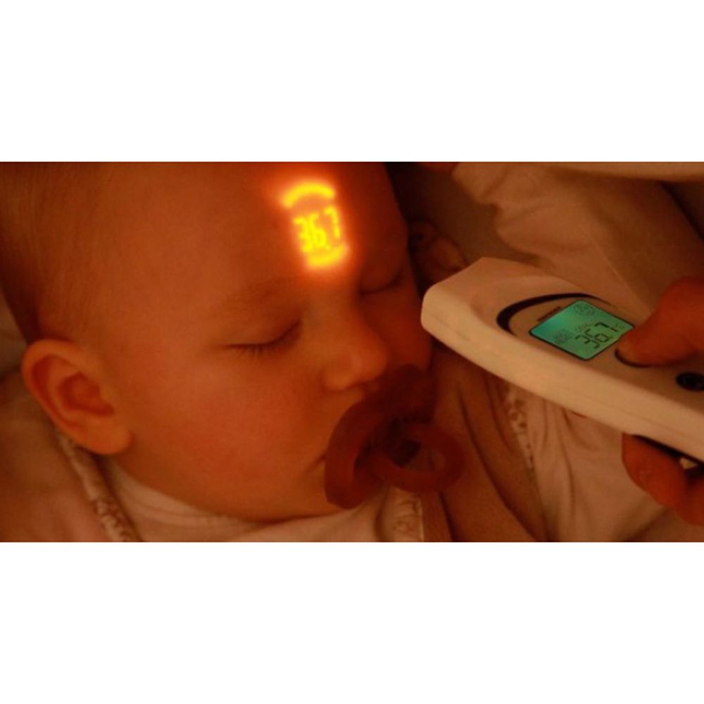 Infrarot-Thermometer misst die Temperatur eines Babys. Das Thermometer wird an der Stirn des Babys gehalten. Das Baby hat einen Schnuller im Mund.