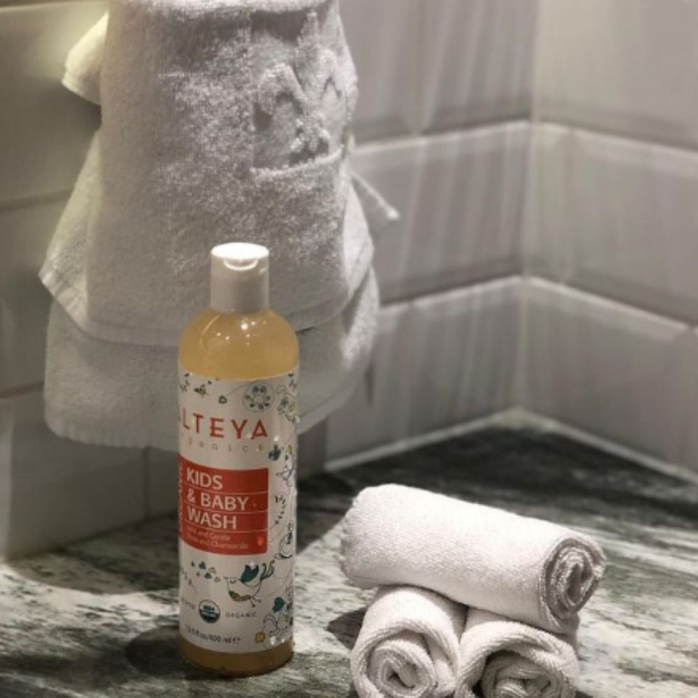 Alteya Organics Kids & Baby Wash. Flasche neben gefalteten Handtüchern. Bad-Szene mit weißen Handtüchern.
