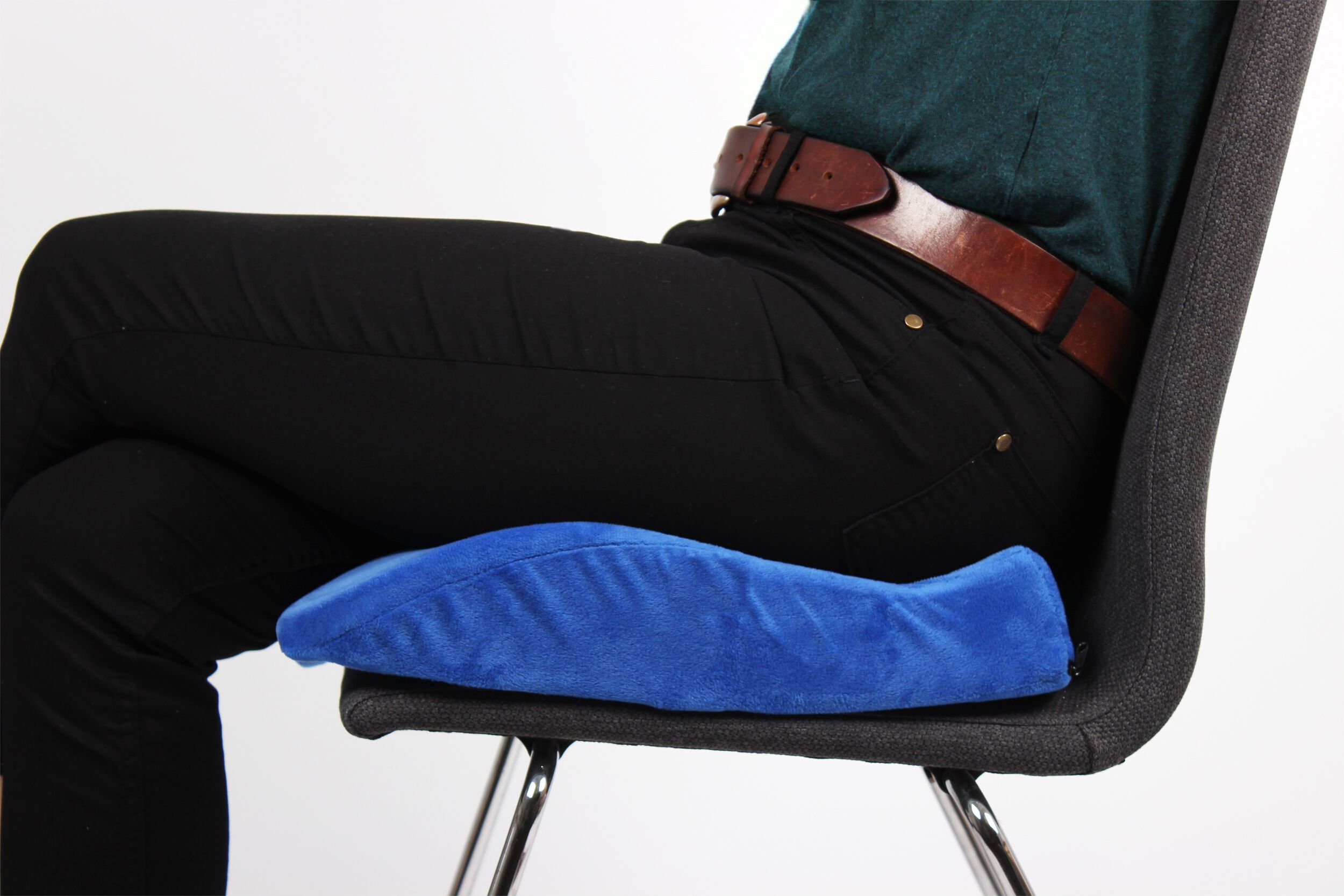 Blaues Sitzkissen auf einem Stuhl. Person sitzt darauf. Brauner Gürtel, schwarze Hose.