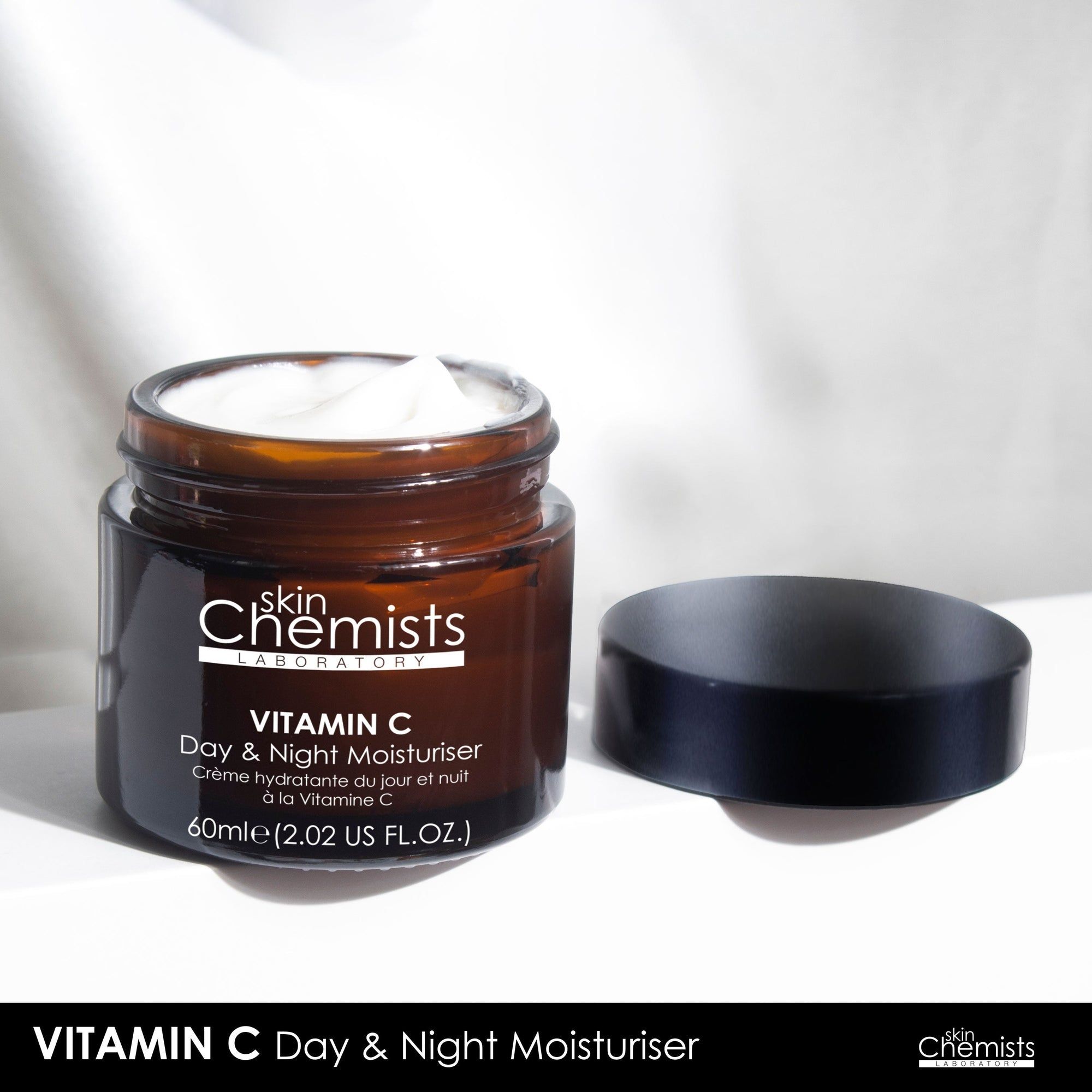 Braune Glasdose mit schwarzem Deckel, geöffnet. Creme sichtbar. Aufschrift: Vitamin C Day & Night Moisturiser. Marke: skinChemists.