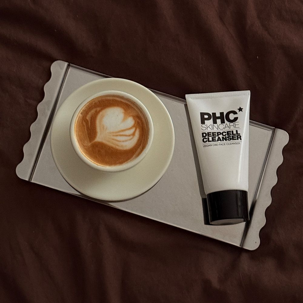 Weiße Tube mit schwarzem Deckel. Aufschrift: PHC Skincare Deepcell Cleanser. Liegt neben einer Tasse Kaffee.