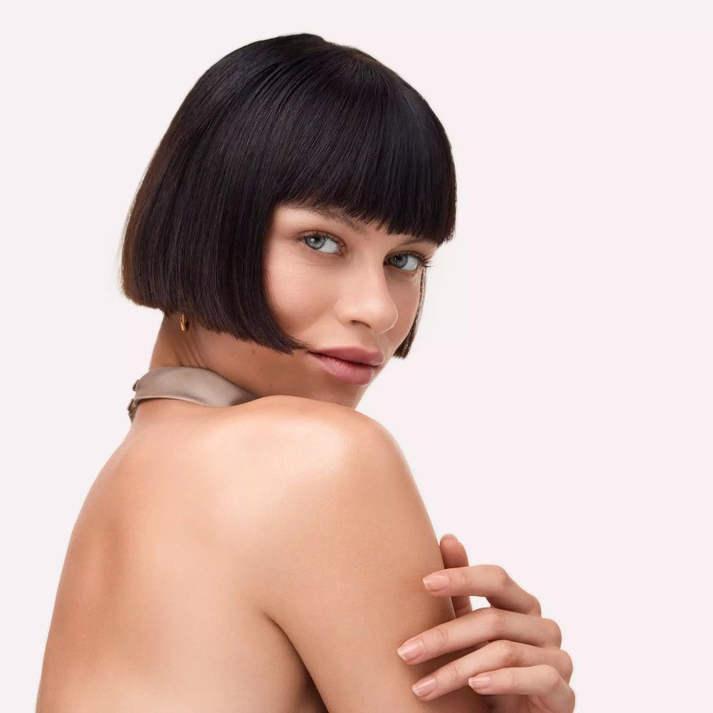 Frau mit Bob-Frisur. Haut glänzt. Trägt Halsband. Blick zur Seite.