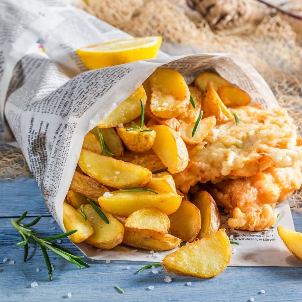 Pommes Frites und Fisch in Zeitungspapier. Zitrone und Rosmarin garnieren das Gericht.