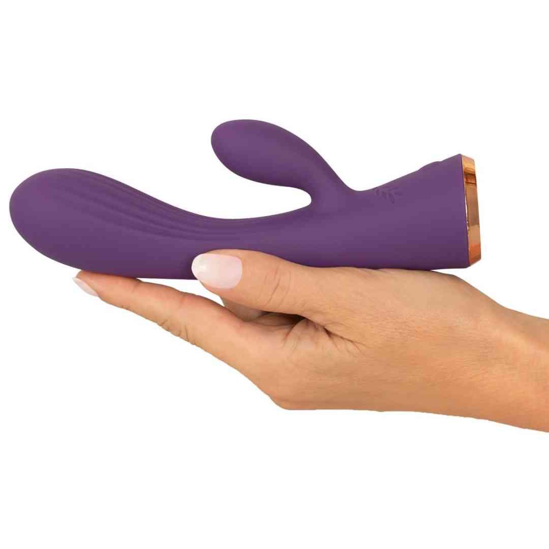 Lila Vibrator in einer Hand gehalten. Goldfarbener Sockel. Glatte Oberfläche. Hasenohren-Design.
