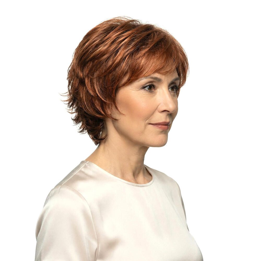 Frau mit rotbrauner Perücke. Dreiviertelansicht. Kurze, gewellte Haare. Helle Haut, weißes Oberteil. Blick zur Seite.