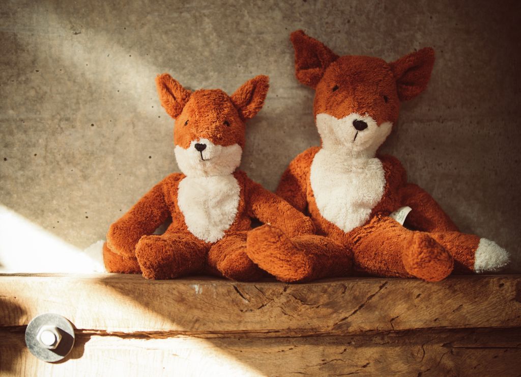 Deux renards en peluche marron et blanc, assis côte à côte. Oreilles dressées, nez noirs.