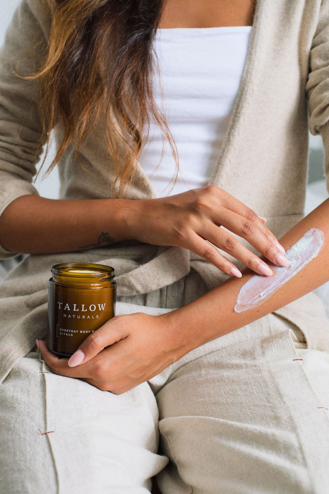 Frau trägt Körperbutter auf den Arm auf. Braune Dose mit schwarzem Deckel. Aufschrift: TALLOW NATURALS, EVERYDAY BODY BUTTER CITRUS.
