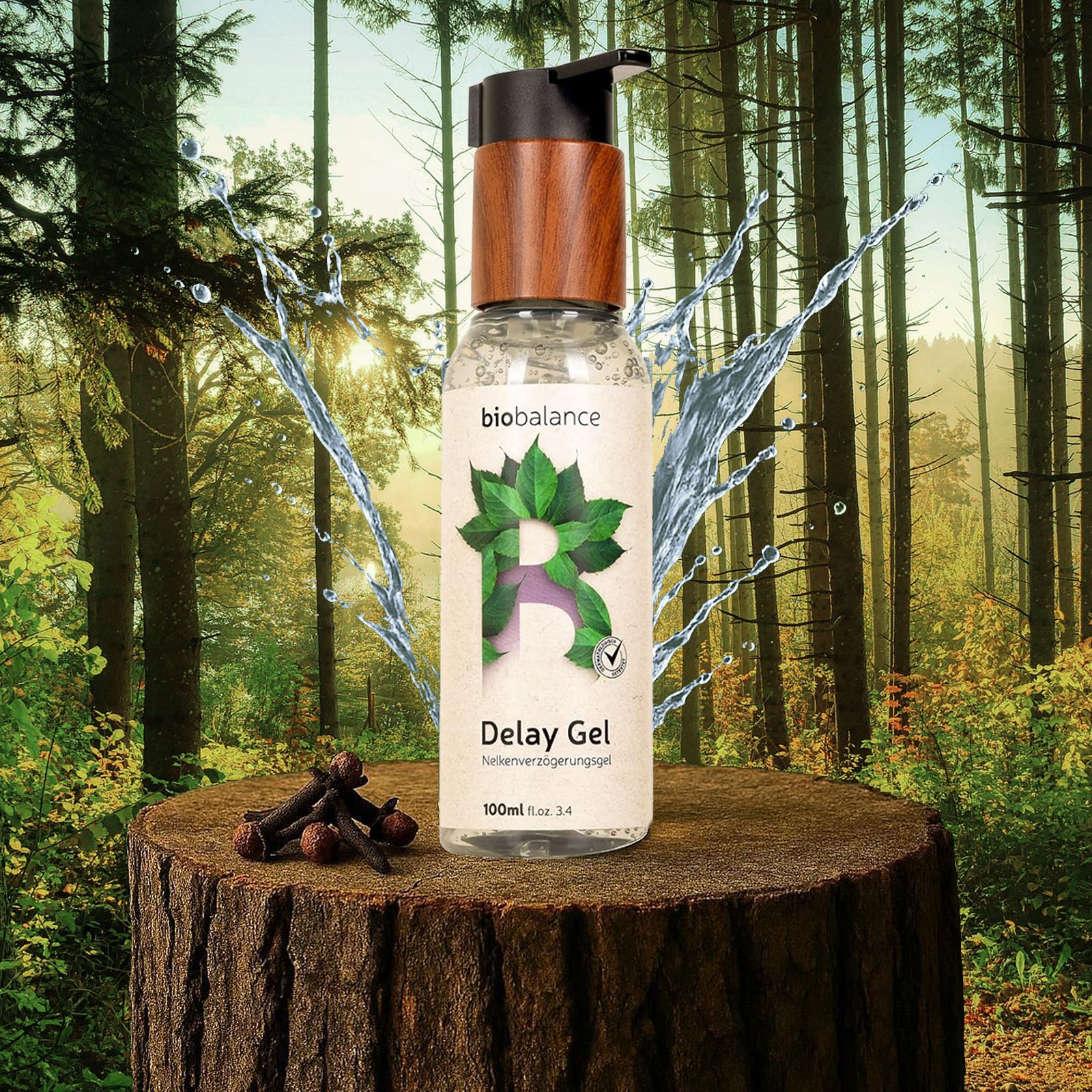 Delay Gel Flasche auf Baumstumpf. Wasser spritzt. Nelken. Waldhintergrund. Holzdeckel. Logo und Produktname sichtbar.