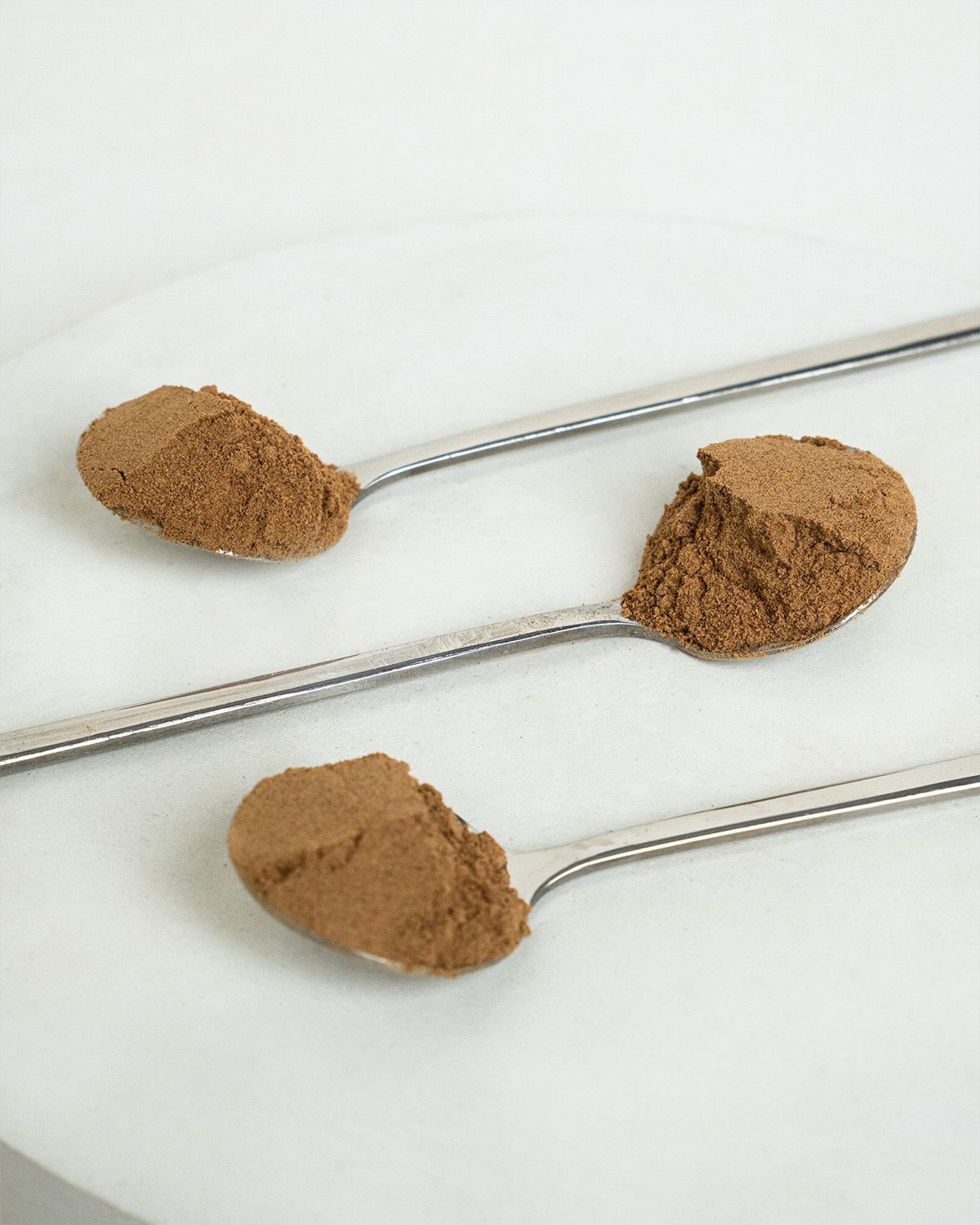 Drei Löffel mit Bio Camu Camu Pulver auf einer runden Marmorplatte.