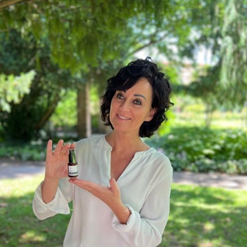 Frau hält Produktflasche. Text: Anti-Aging Eye Contour Cream. Hintergrund: grüner Baum, sonniger Tag.