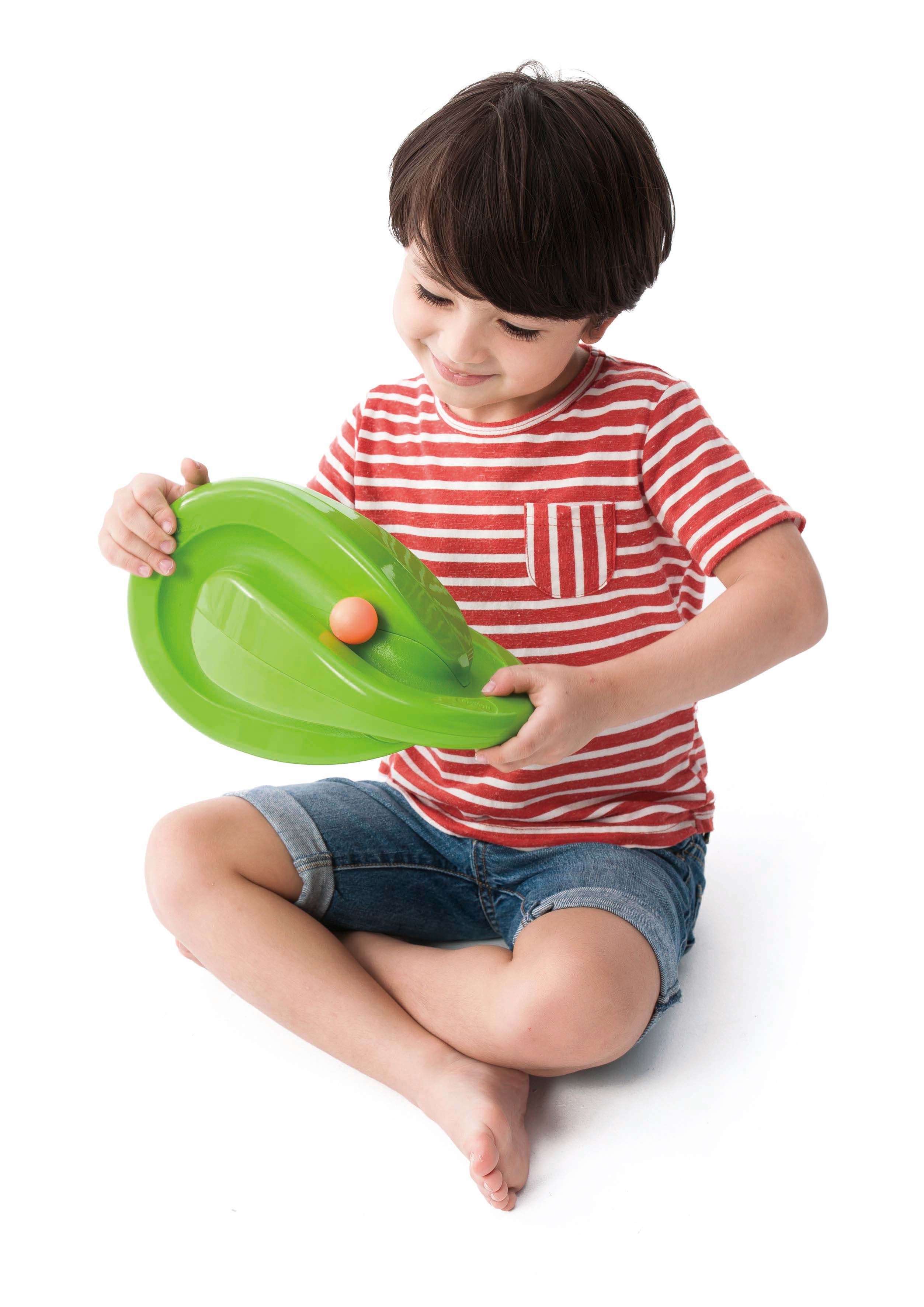 Ein Kind sitzt und hält ein grünes, geschwungenes Spielgerät mit einer orangefarbenen Kugel. Kind trägt ein rot-weiß gestreiftes T-Shirt.