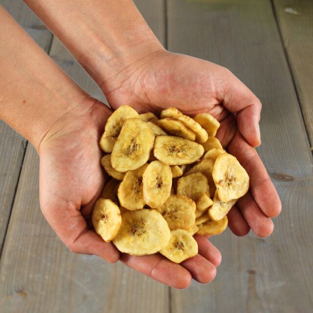 Getrocknete Bananenscheiben in Händen. Goldgelbe Farbe, runde Form.