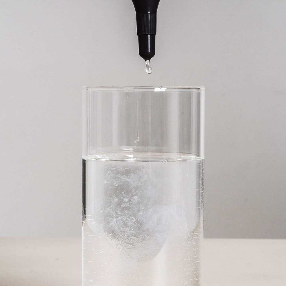 Glas mit Wasser, Tropfen aus schwarzem Applikator. Flüssigkeit vermischt sich im Wasser.