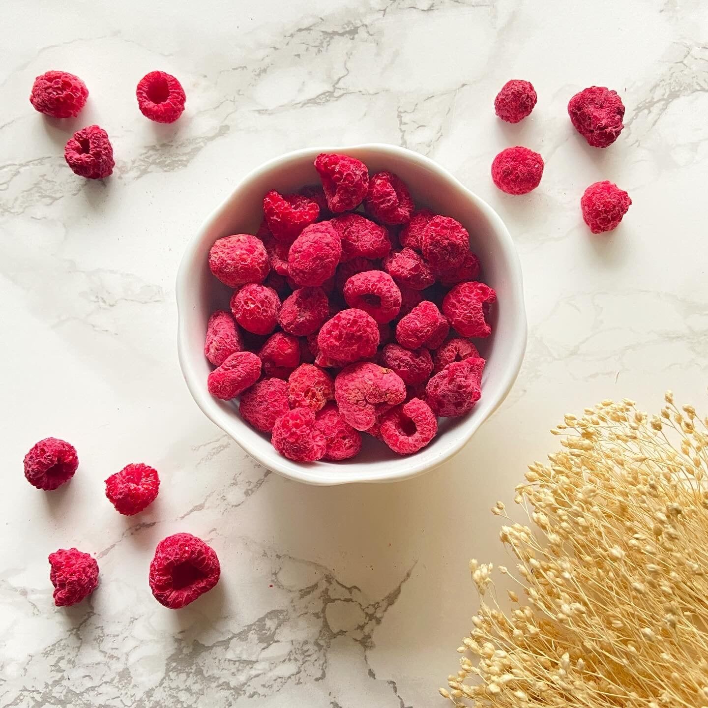 Himbeeren in einer weißen Schale. Einige Beeren verstreut. Draufsicht auf hellem Hintergrund.