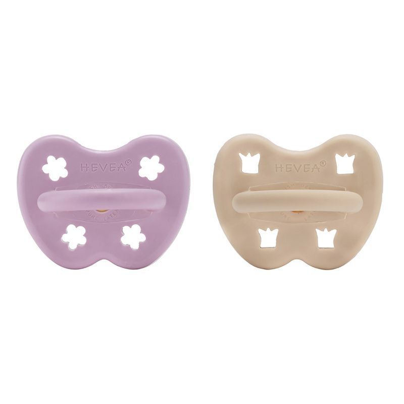 Zwei Schnuller, lila und beige. Anatomische Form mit HEVEA-Logo. Blütenförmige Öffnungen.
