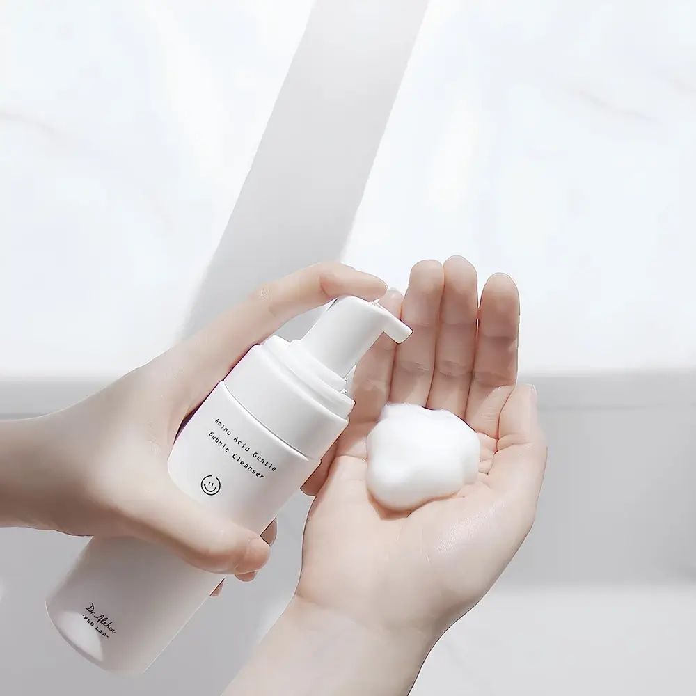 Hände halten eine weiße Flasche und Schaum. Aufschrift: Amino Acid Gentle Bubble Cleanser. Marke: Dr. Althea.