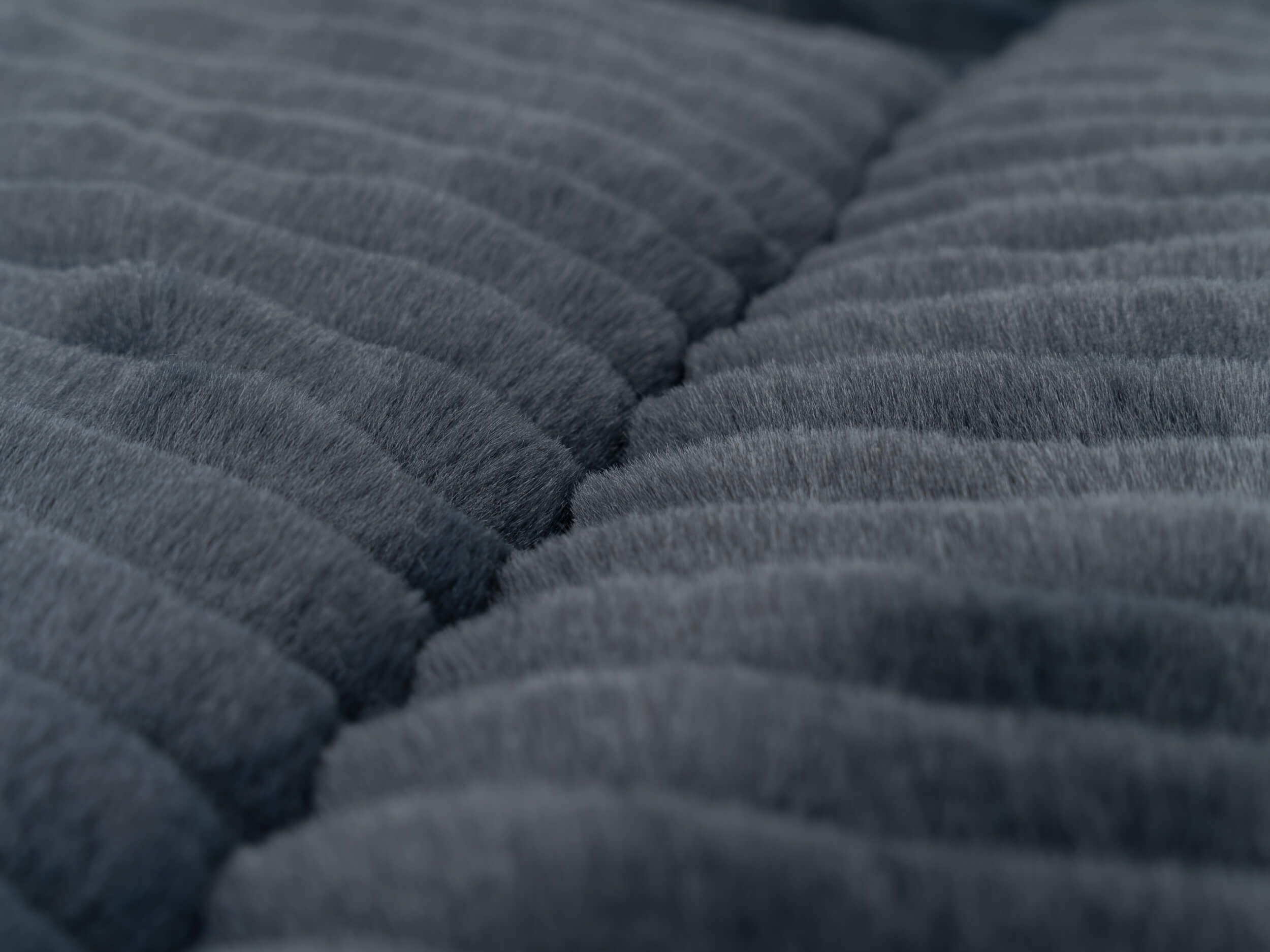Gefütterte Liegedecke, grau, mit geriffelter Oberfläche. Nahaufnahme, Texturdetails sichtbar.