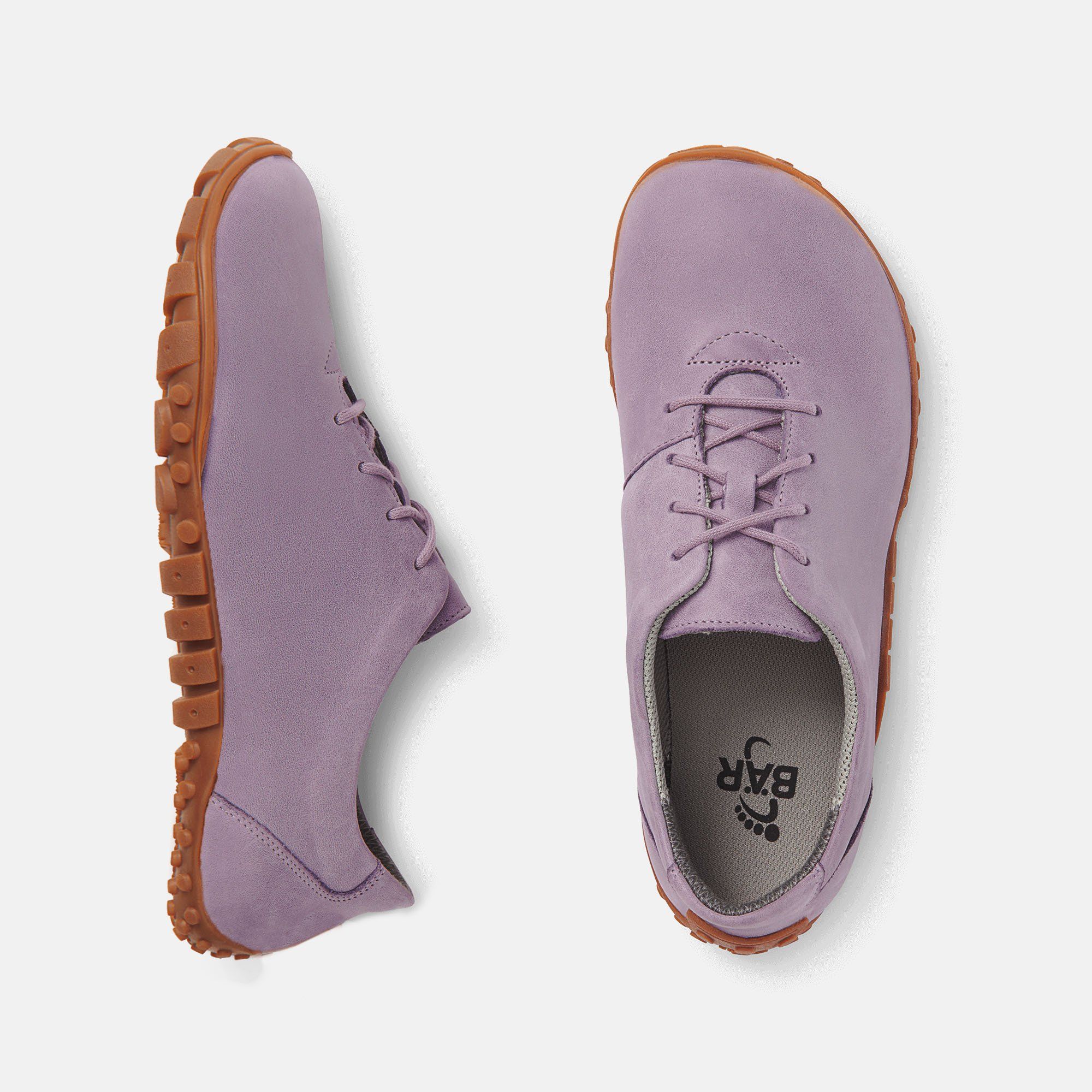 Zwei lilafarbene Schnürschuhe mit brauner Sohle. Breite Passform. Innensohle mit Logo. Hellgrauer Hintergrund.