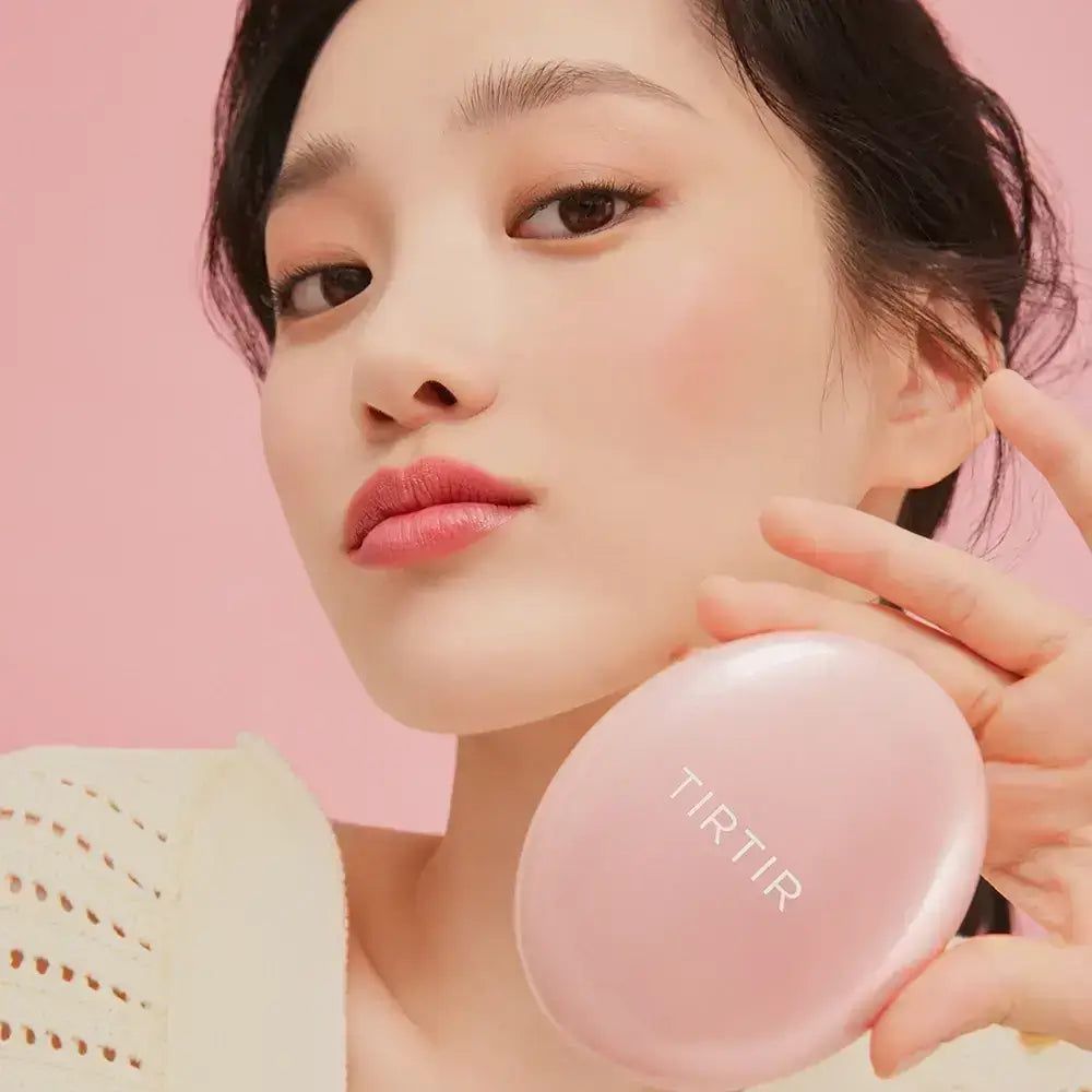 Frau hält ein rosa Make-up-Kompaktpuder. Das Produkt ist mit „TIRTIR“ beschriftet. Die Frau hat Make-up aufgetragen.