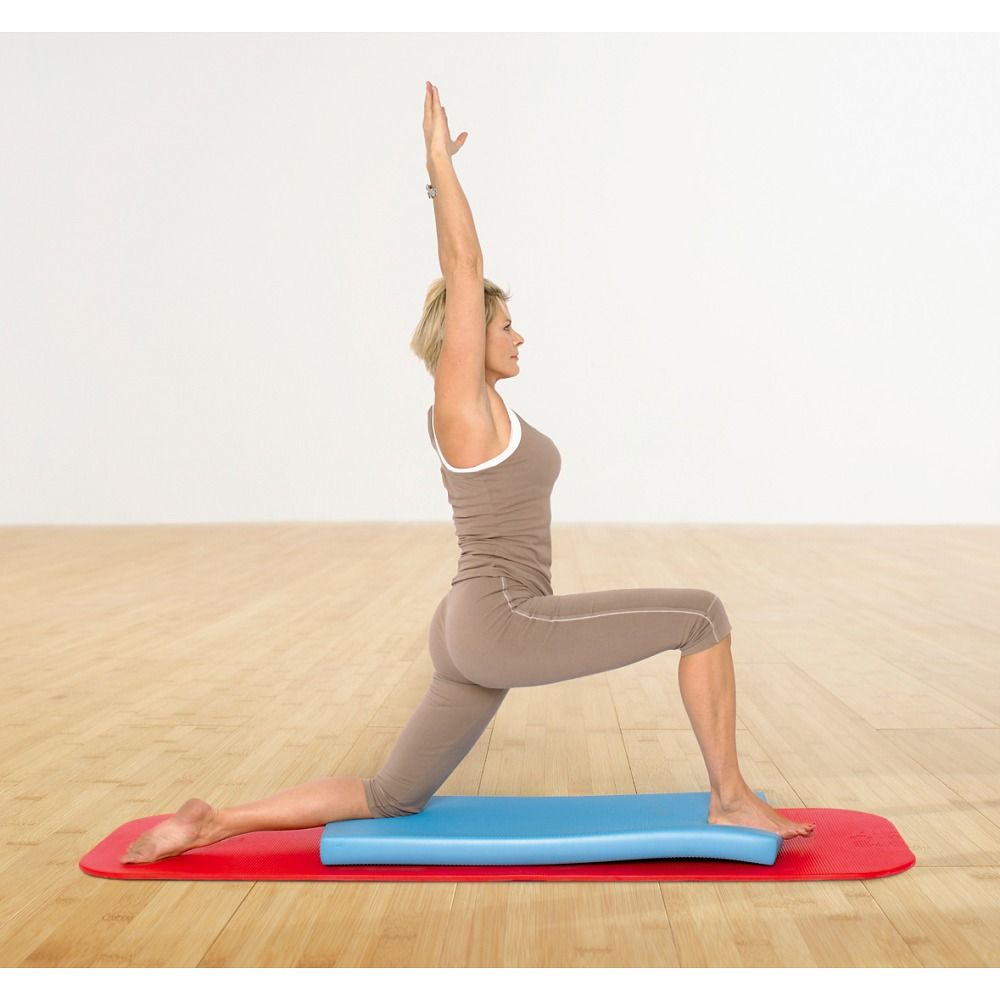 Frau in Yoga-Pose auf roter Matte mit blauem Balance-Pad. Arme nach oben gestreckt, rechtes Bein angewinkelt.