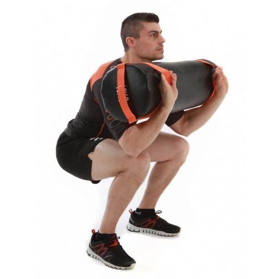 Mann in Sportkleidung hockt mit Power Bag. Schwarzer Sack mit orangefarbenen Griffen.