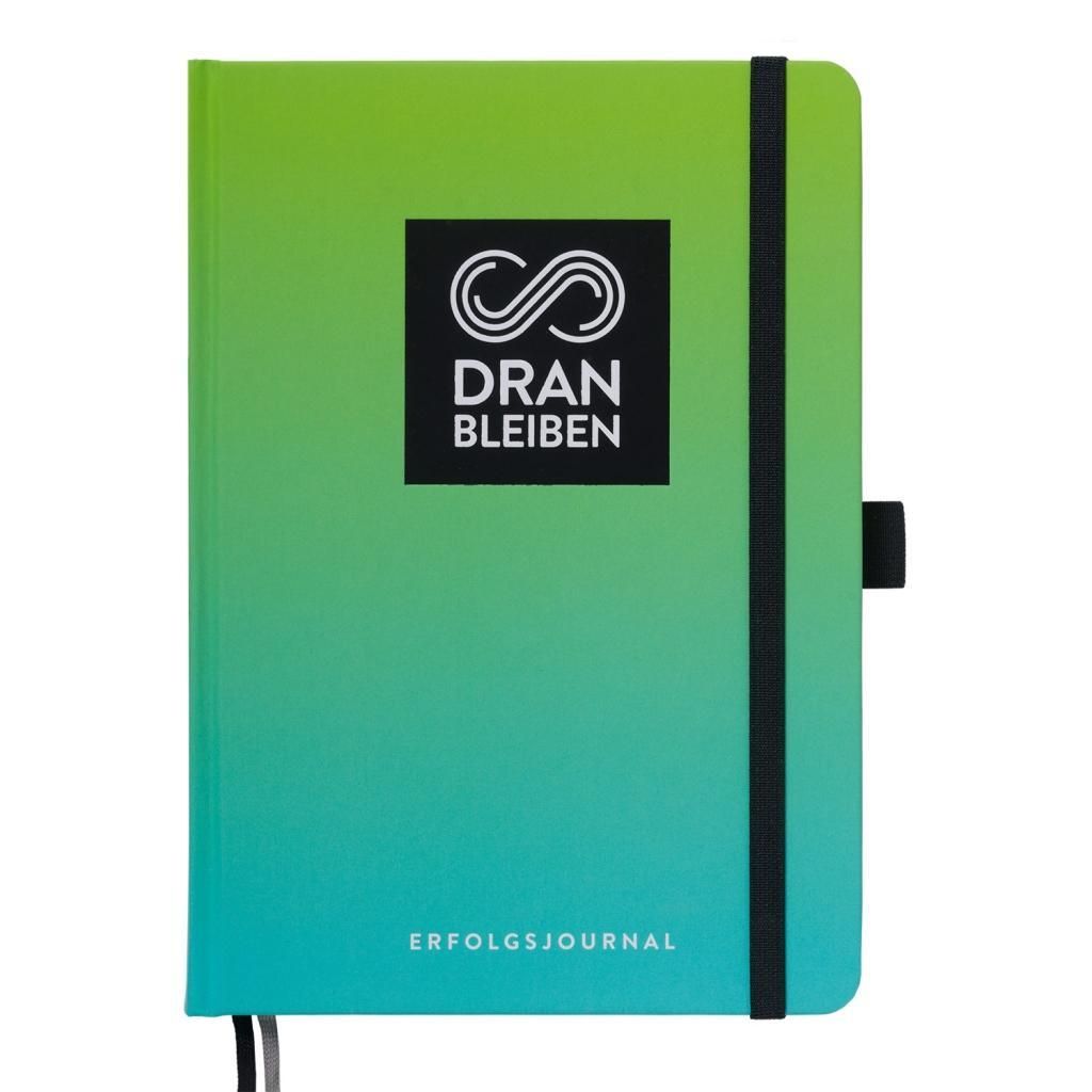 Journal mit grün-blauem Farbverlauf. Schwarzes Gummiband und Verschluss. Logo und Schriftzug 'DRAN BLEIBEN'.