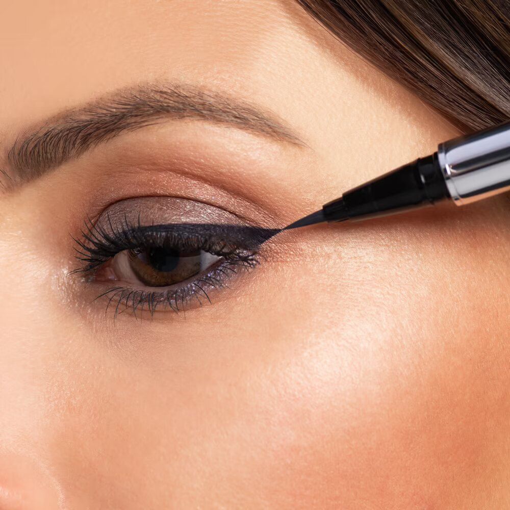 Nahaufnahme eines Auges, das mit einem schwarzen Eyeliner geschminkt wird. Der Eyeliner ist sichtbar.