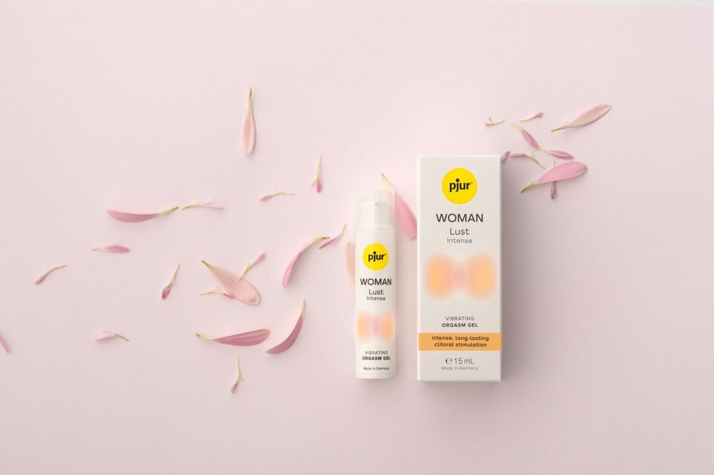 Pjur Woman Lust Intense Vibrating Orgasmusgel. Flasche und Verpackung. Auf rosa Untergrund mit Blütenblättern. Text: intense, long-lasting clitoral stimulation.