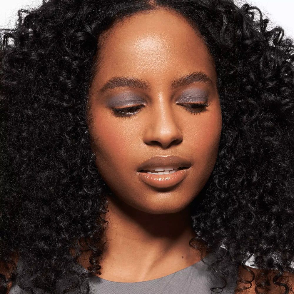 Porträt einer Frau mit Lippenstift. Sie schaut nach unten. Graues Oberteil.