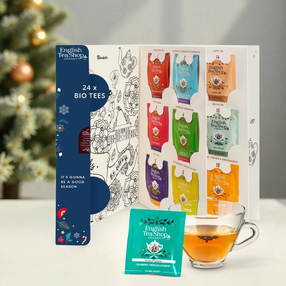 Geöffnete Adventskalender-Box mit 24 Teebeuteln. English Tea Shop Logo. Eine Tasse Tee daneben. "24 x BIO TEES" Text.